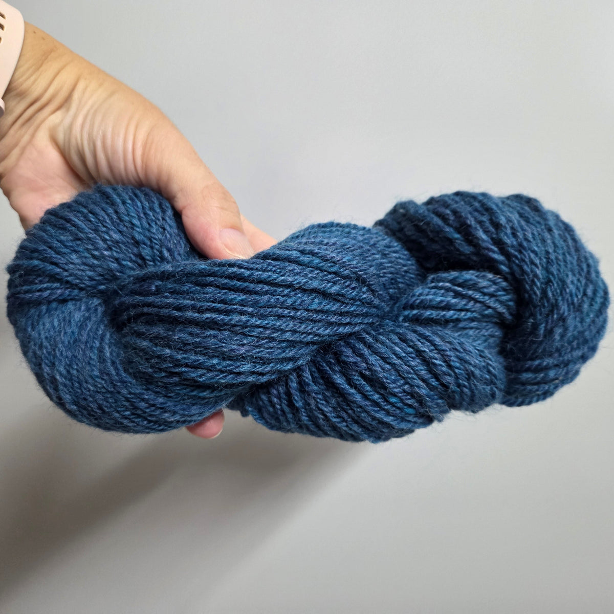 Hand holding a skein of blue yarn against a neutral background