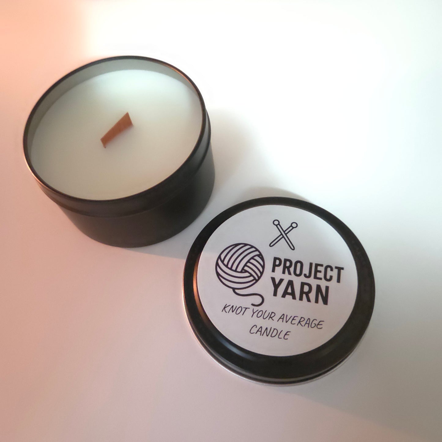 Candle in a tin with 'Project Yarn' branding on a light background