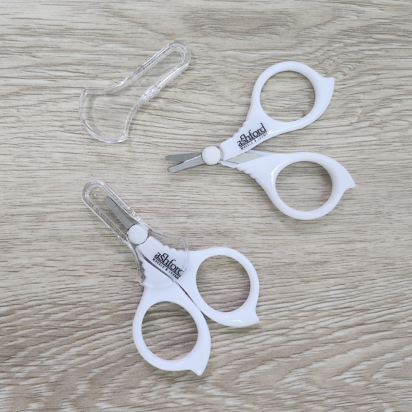 Pair of white Ashford Little scissors on a wooden surface