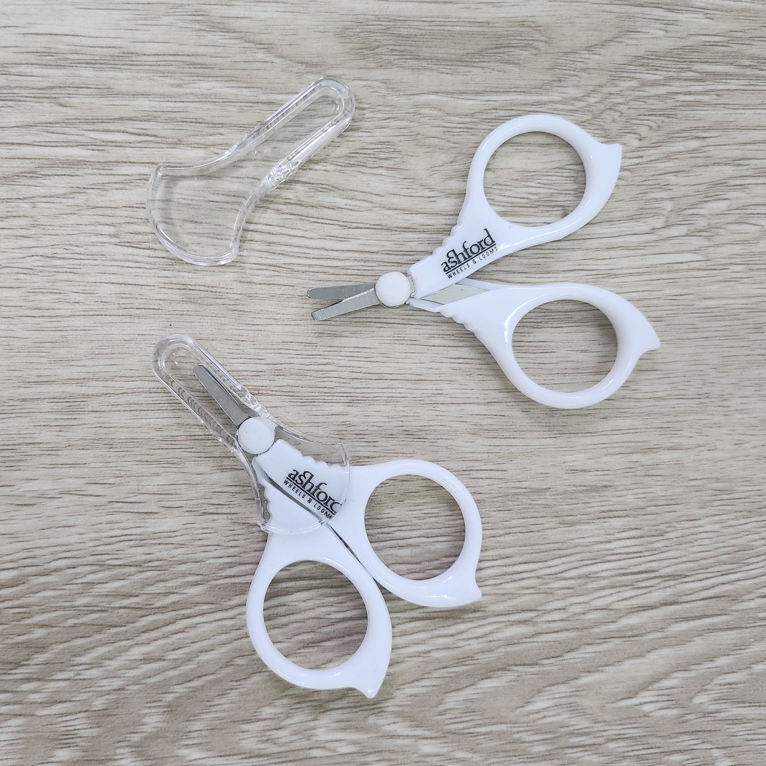 Pair of white Ashford Little scissors on a wooden surface
