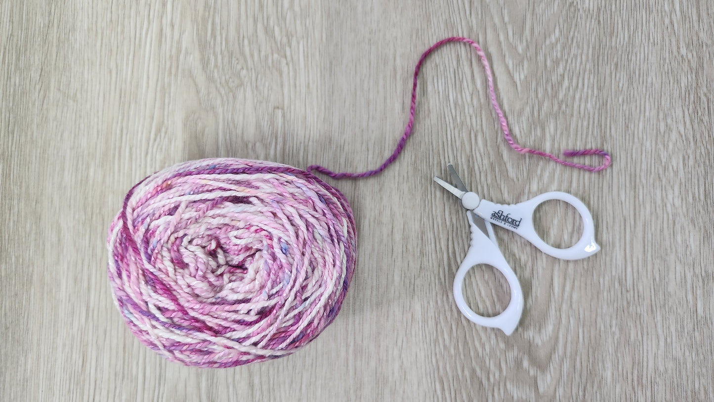 Ball of pink and white yarn with a pair of Ashford Little scissors on a wooden surface