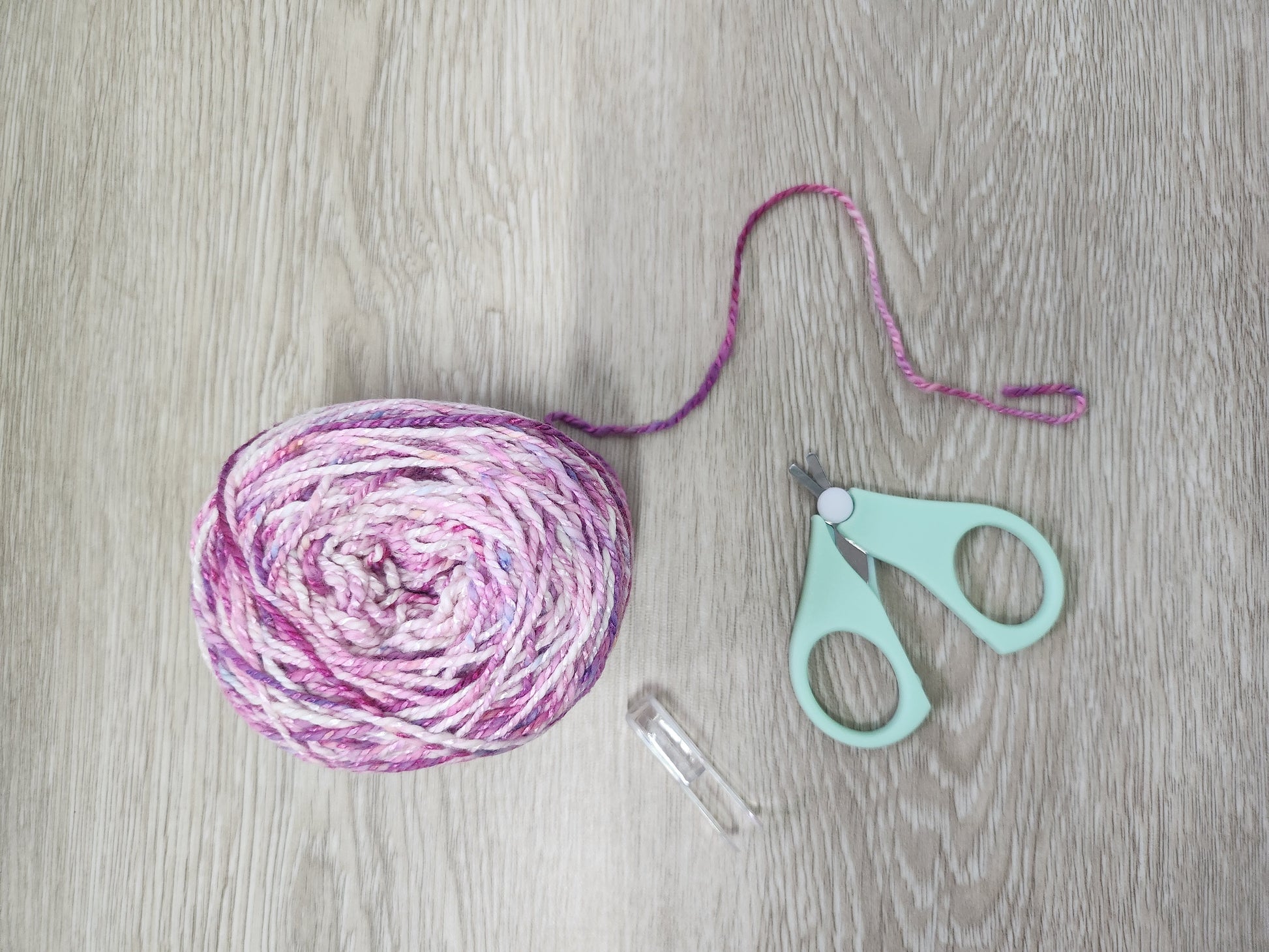 Ball of pink and purple MoYa yarn with small safety scissors on a wooden surface