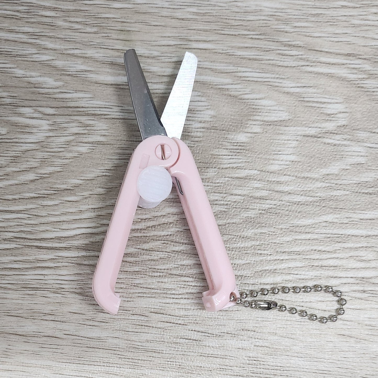 Pink foldable retractable scissors on a wooden surface
