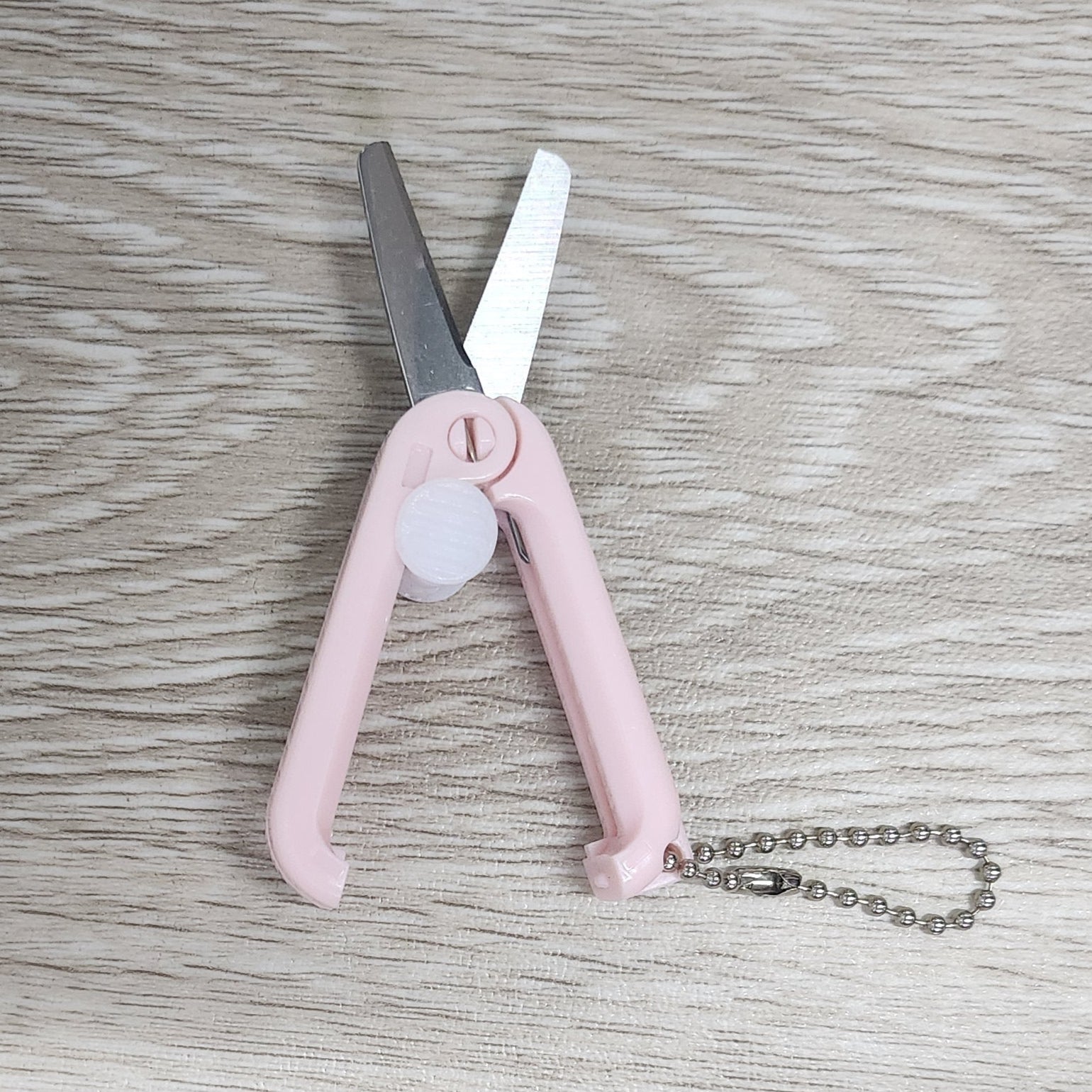 Pink foldable retractable scissors on a wooden surface