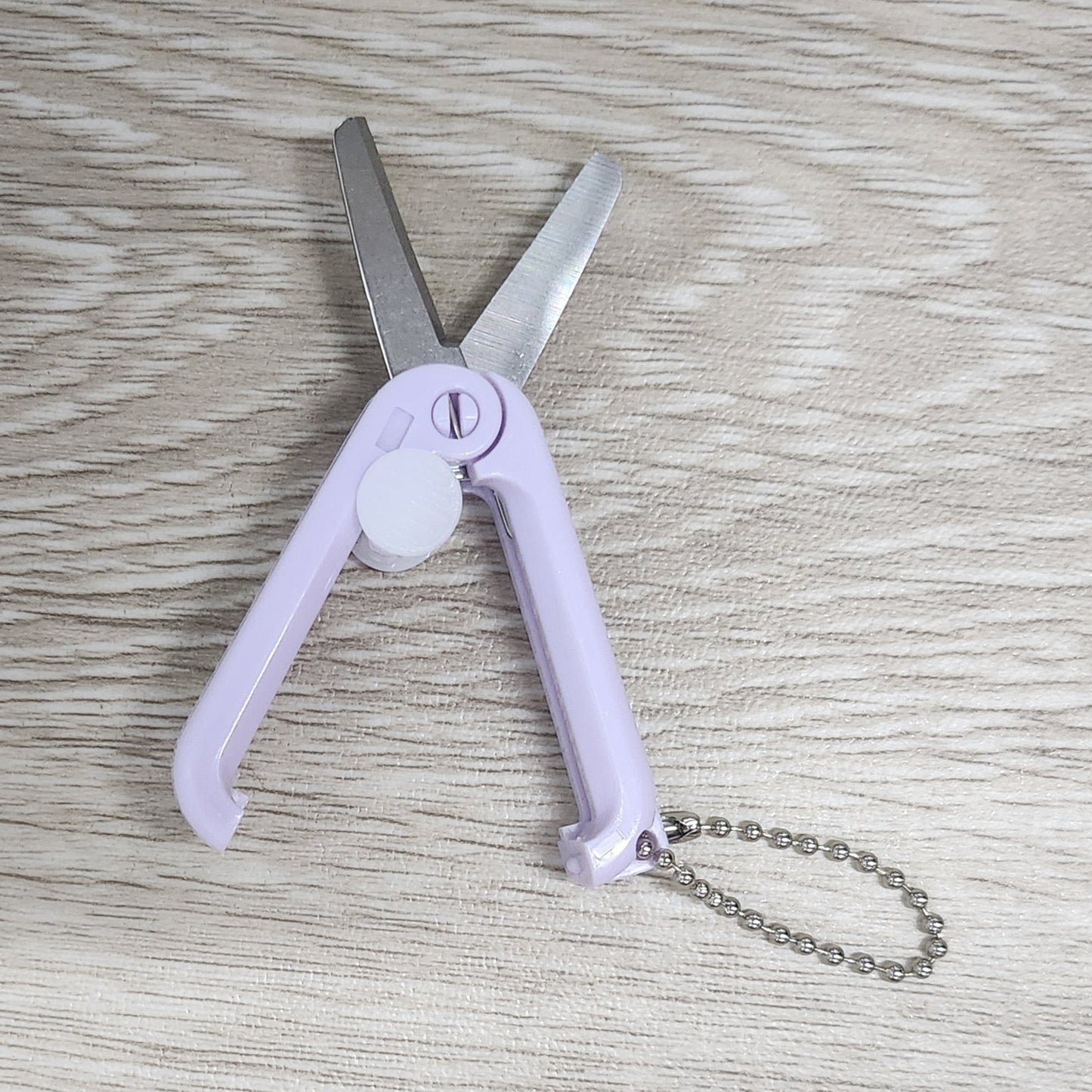 Foldable scissors with a keychain on a wooden surface