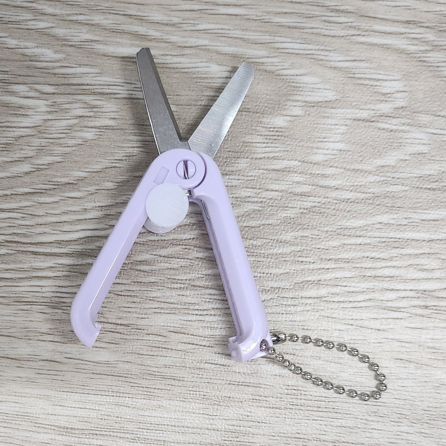 Foldable scissors with a keychain on a wooden surface