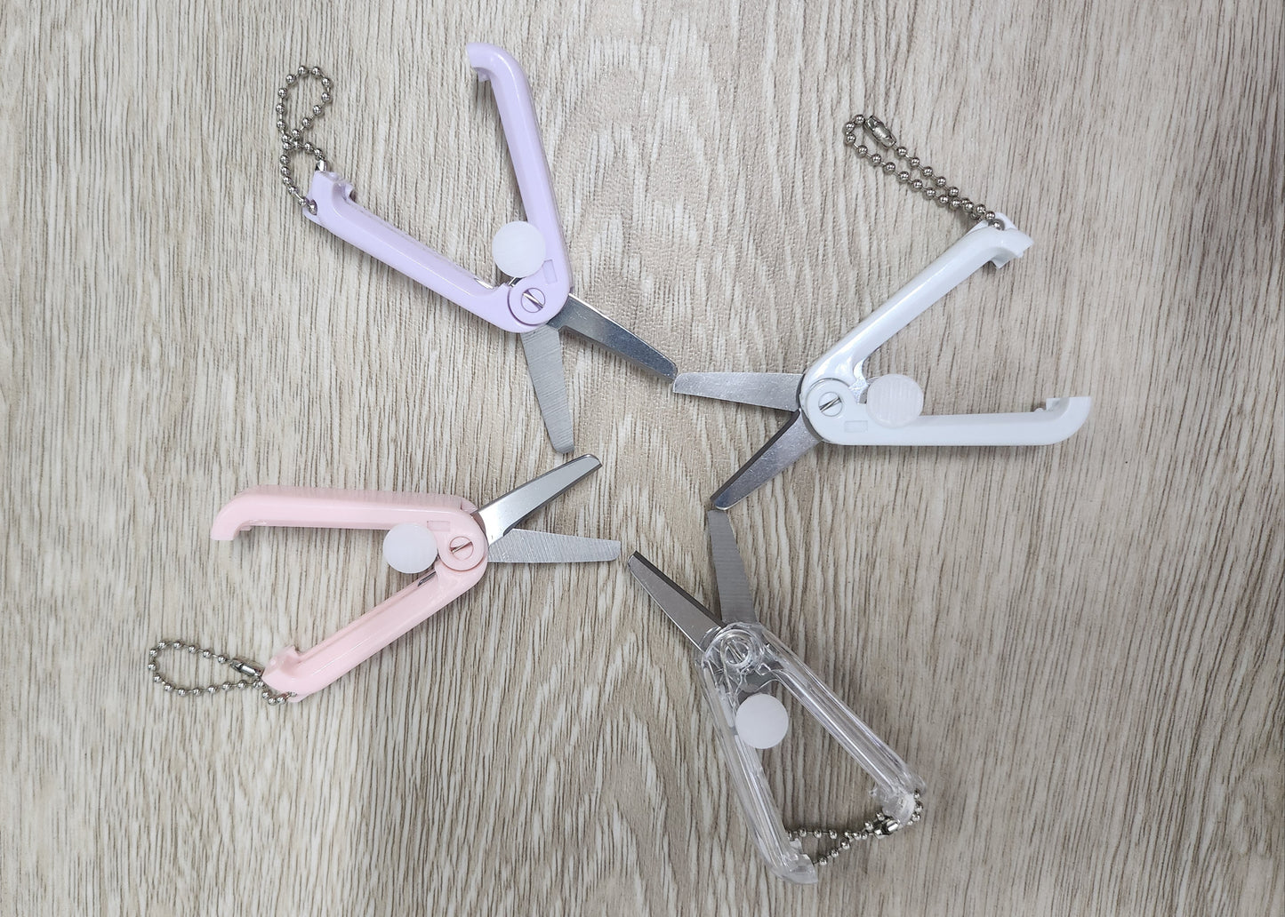 Set of four small foldable retractable scissors with chains on a wooden surface