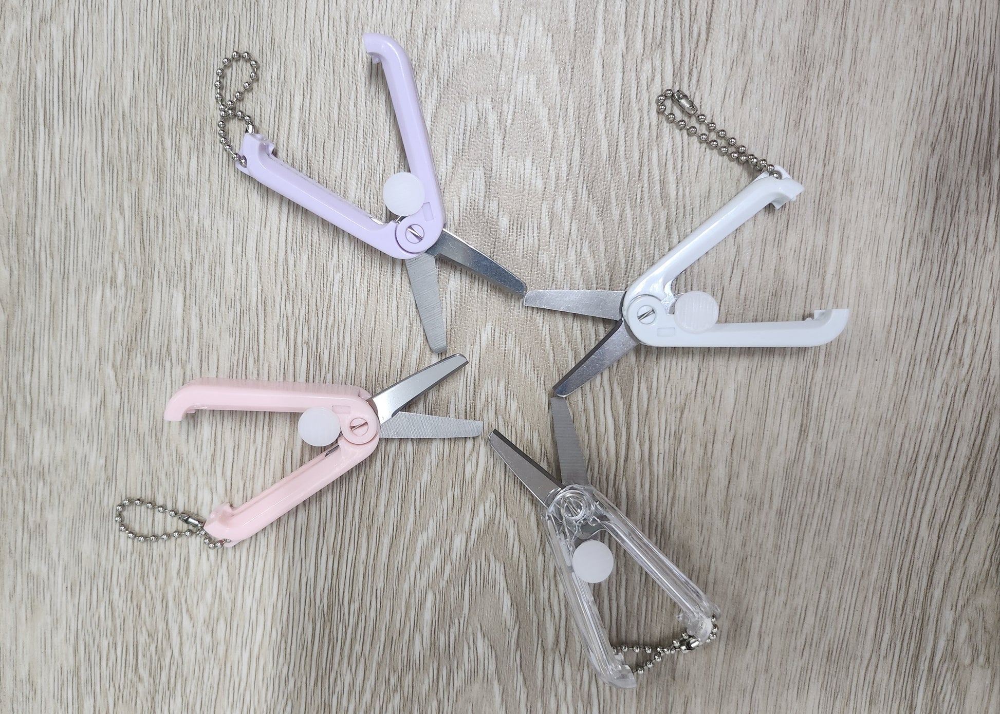 Set of four small foldable retractable scissors with chains on a wooden surface