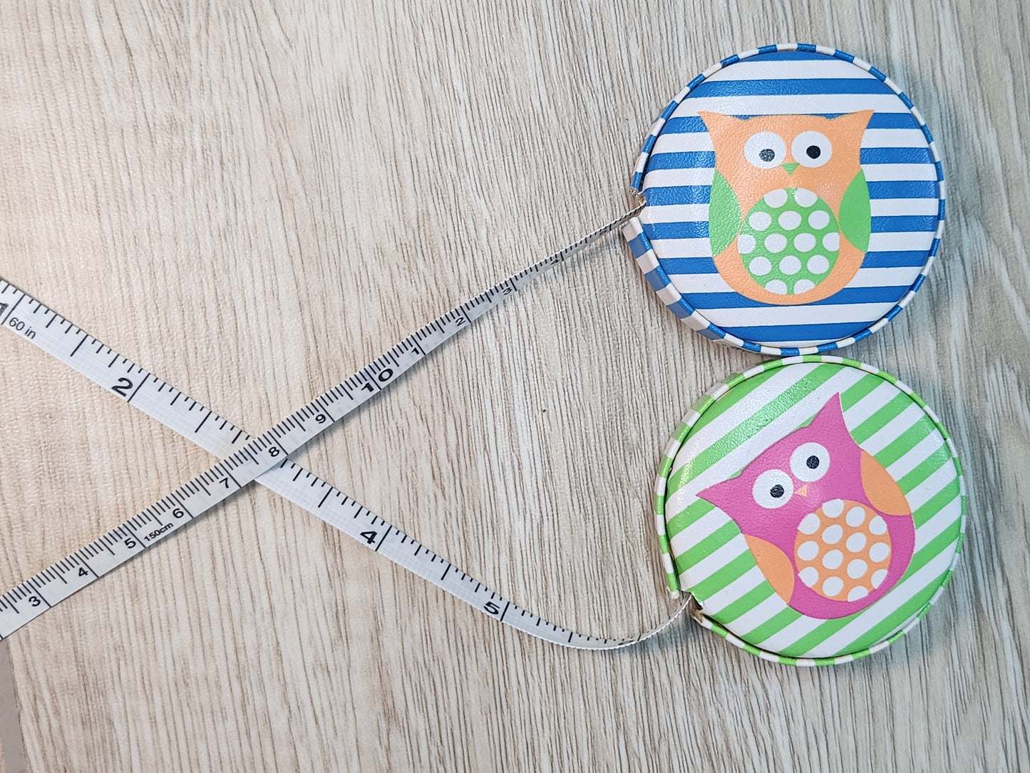 Two fabric-wrapped measuring tapes with owl designs on a wooden surface