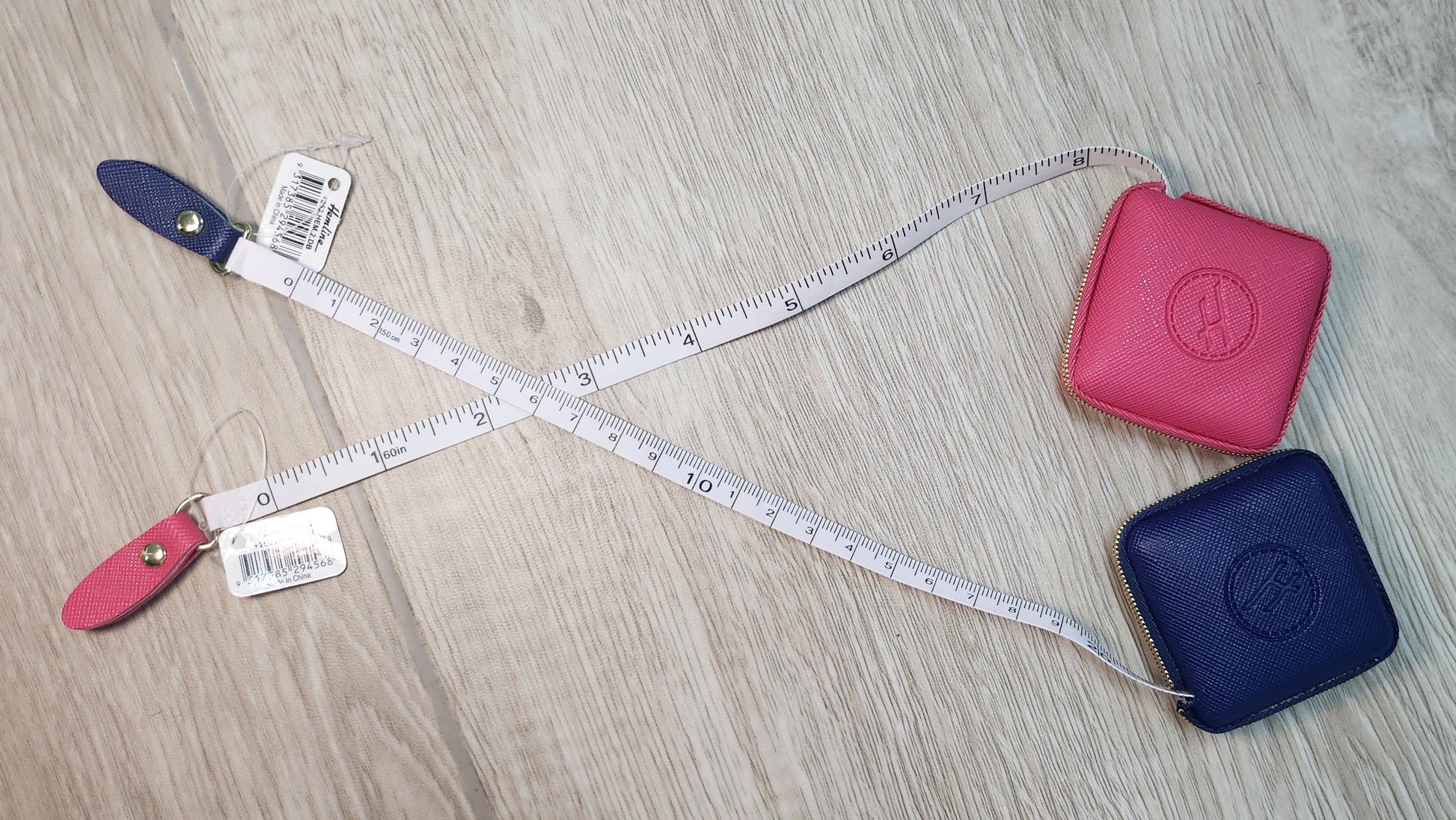 Two measuring devices, a blue and a pink one, with a tape measure on a wooden surface.