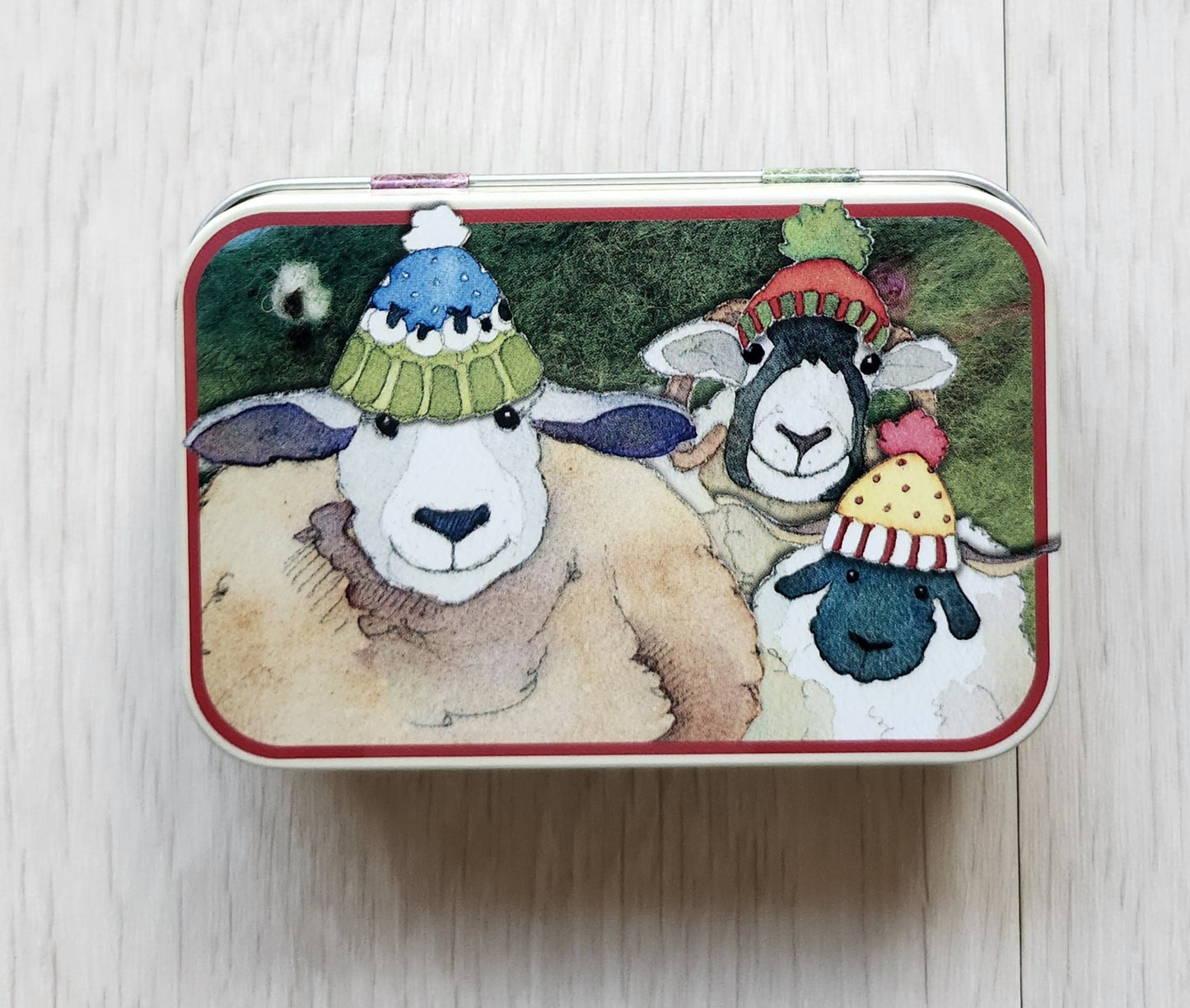 Small rectangular tin with cartoon character design on a light wooden surface emma ball hinged notions tin