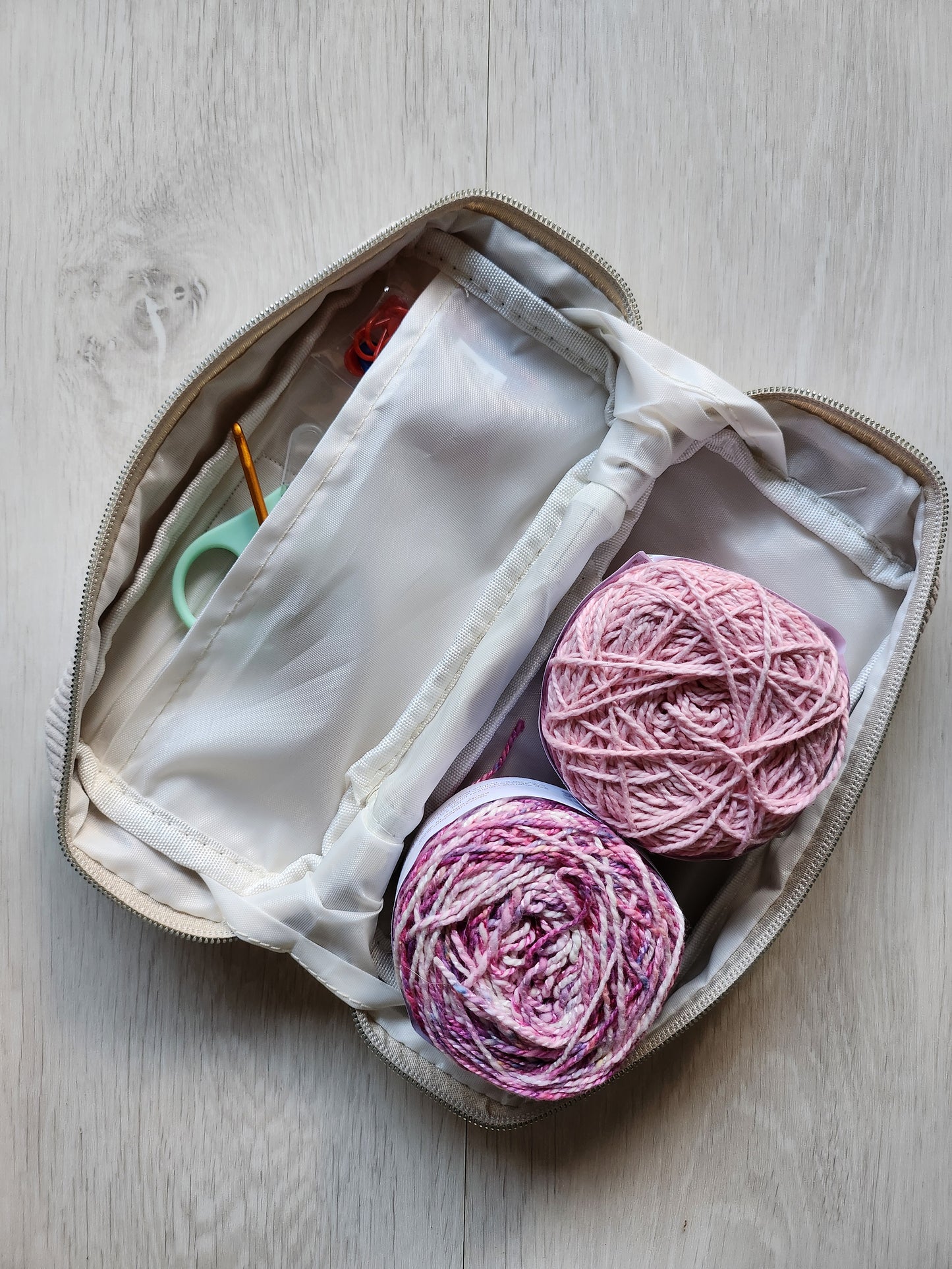 Open pouch containing pink yarn balls and knitting needles on a wooden surface