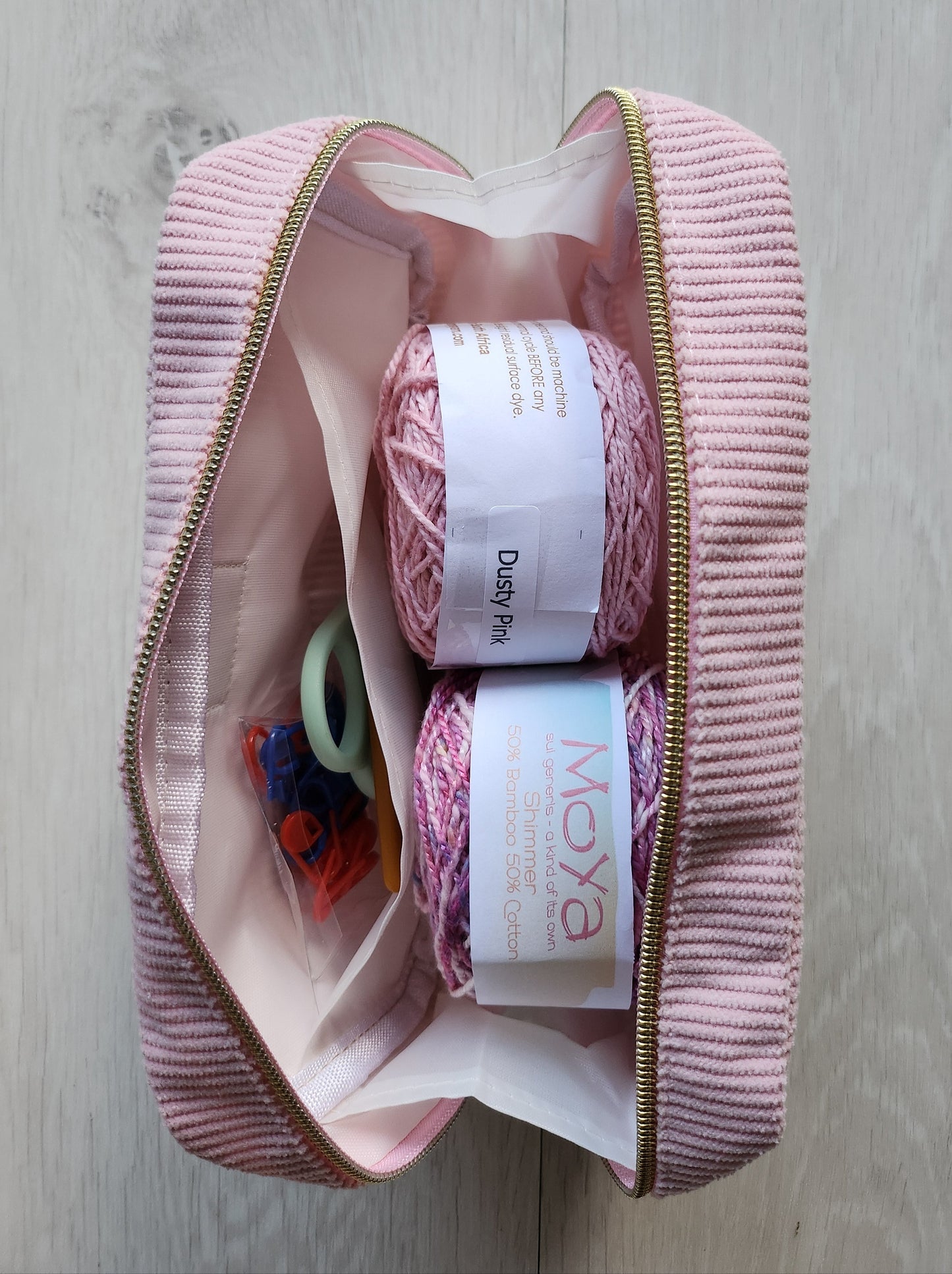 Pink sewing kit with yarn and tools on a light wooden surface