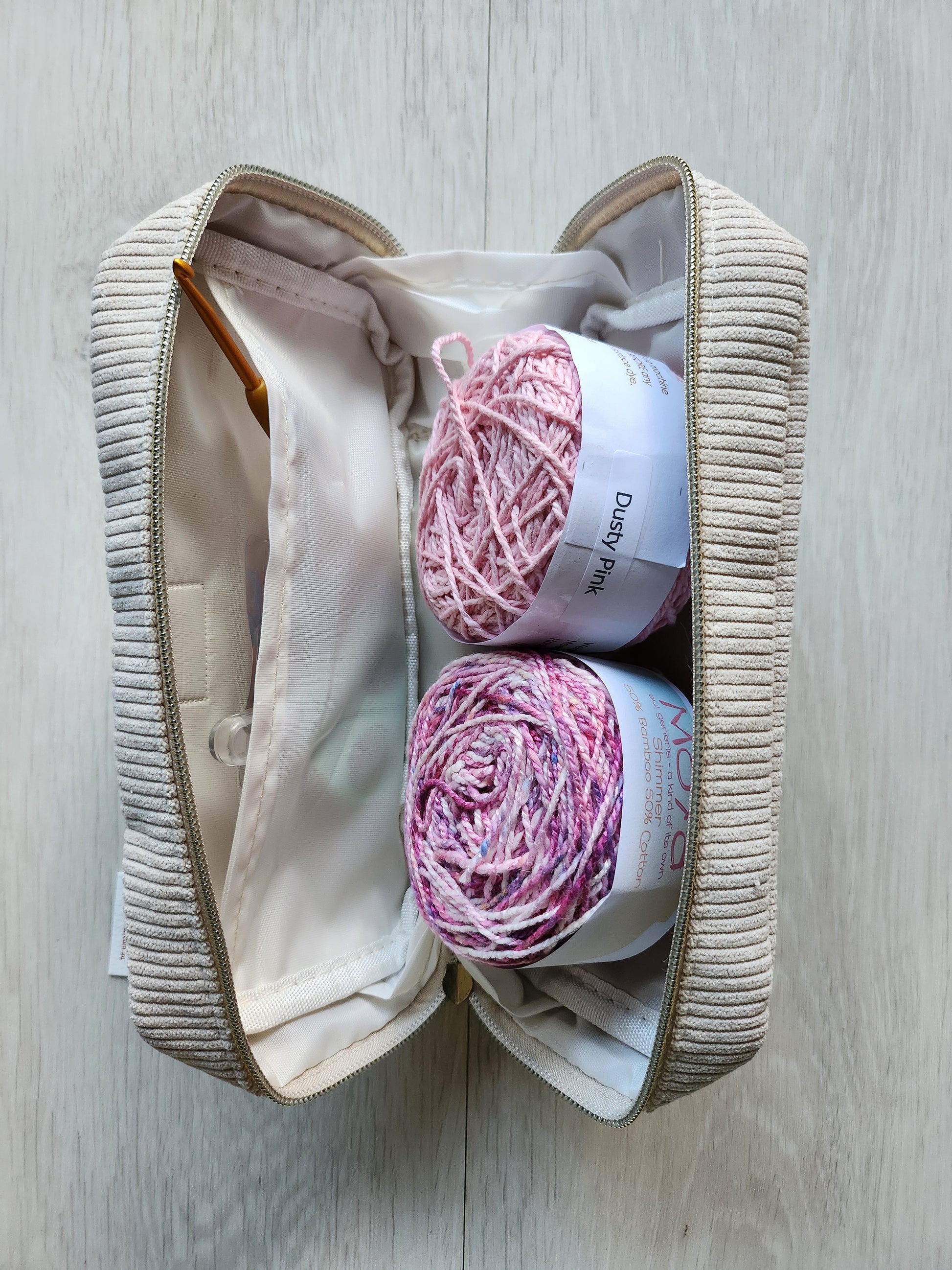 Two balls of pink yarn in a beige yarn bag on a wooden surface