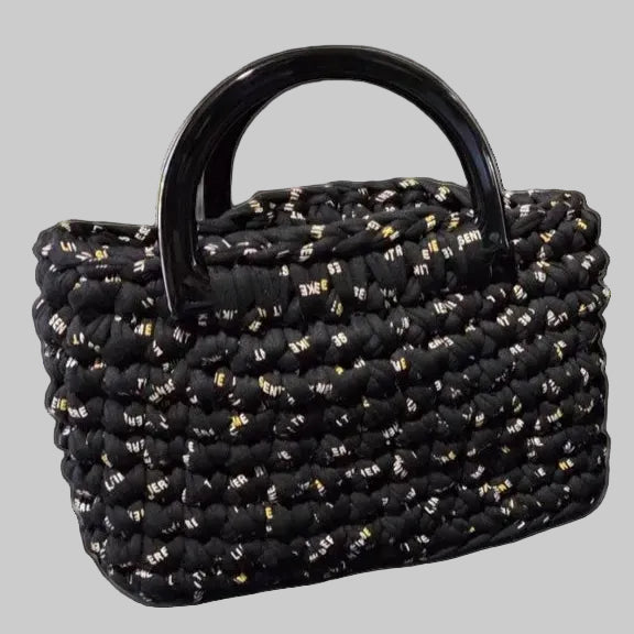 Two woven black handbags with metallic gold speckles, one small with a black handle and one larger with white handles, shown on a light cream background with a small matching pouch in front.