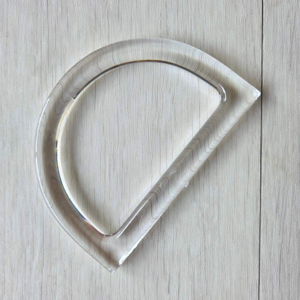 A clear acrylic cookie cutter with a wavy marbled pattern, shown on a light wood background.