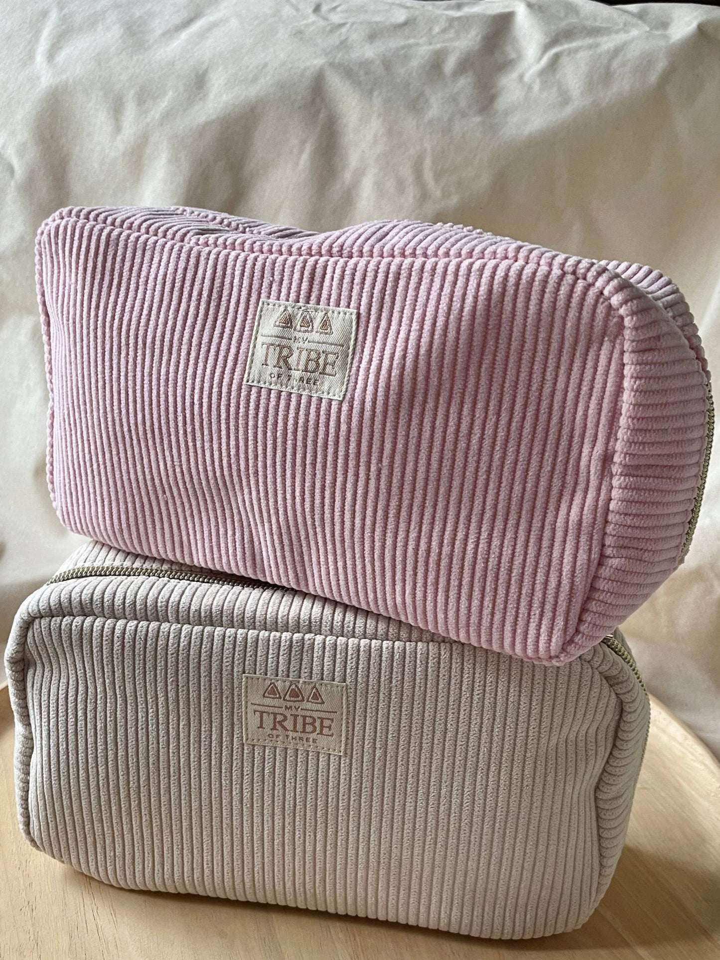 Two corduroy bags, one pink and one beige, on a wooden tray with a white background.