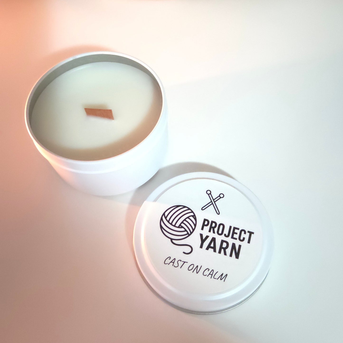 Candle in a tin with 'Project Yarn' branding on a light background