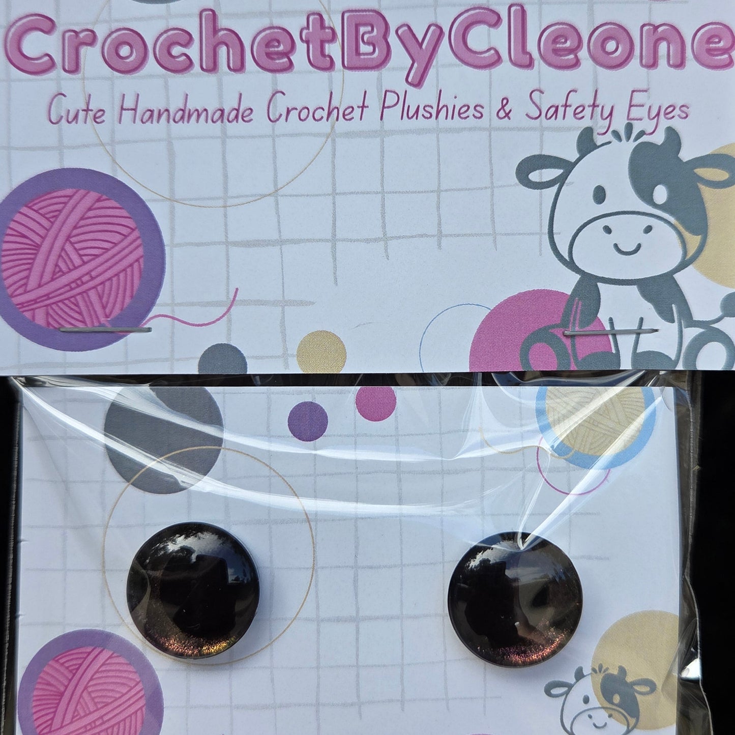 A pair of round black crochet safety eyes in a clear plastic sleeve, attached to a printed display card for 'CrochetByCleone', set against a rustic wooden background.
