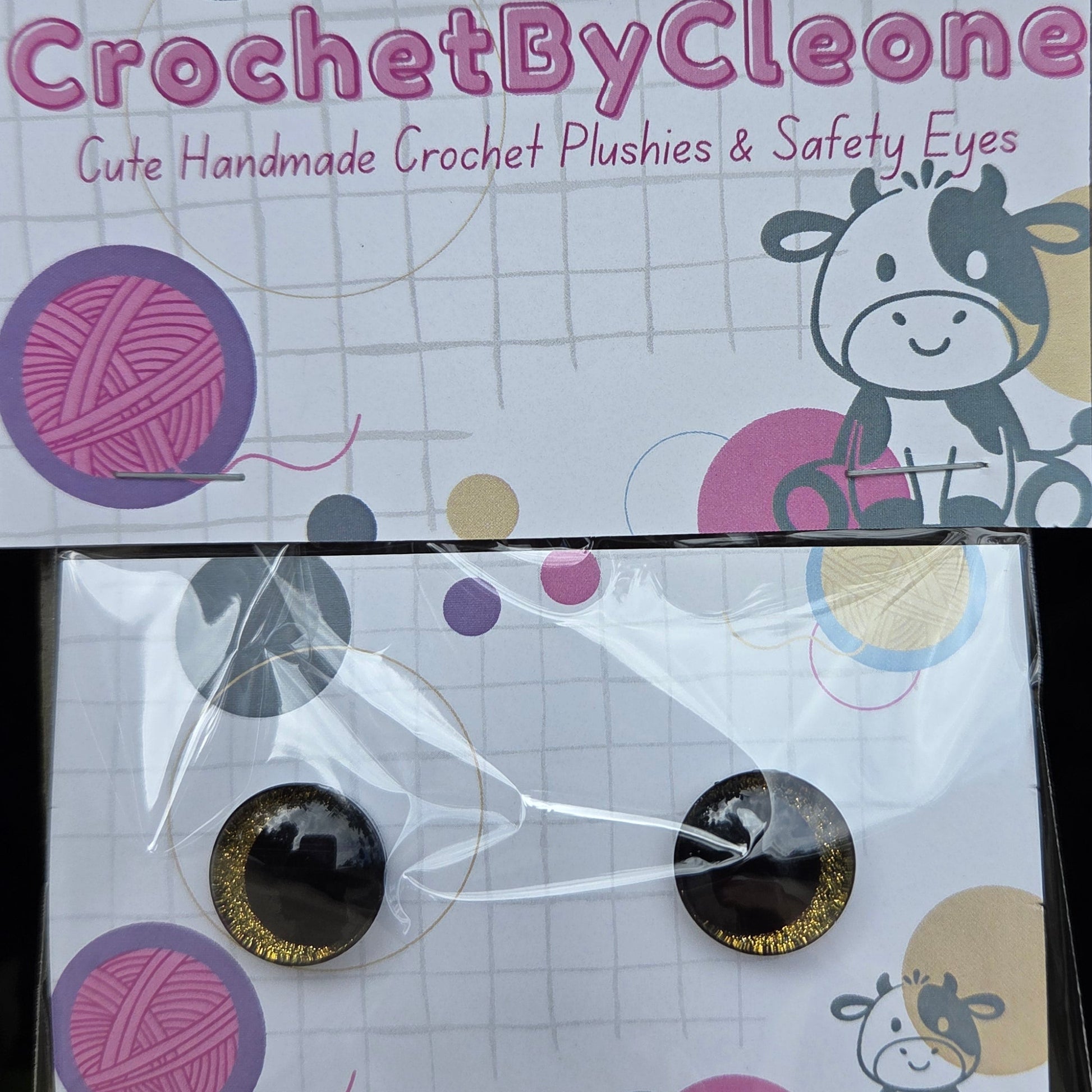 Two round crochet pushins with black and gold glitter centers, packaged on a white card with crochet-themed graphics and the brand name 'CrochetByCleo'.