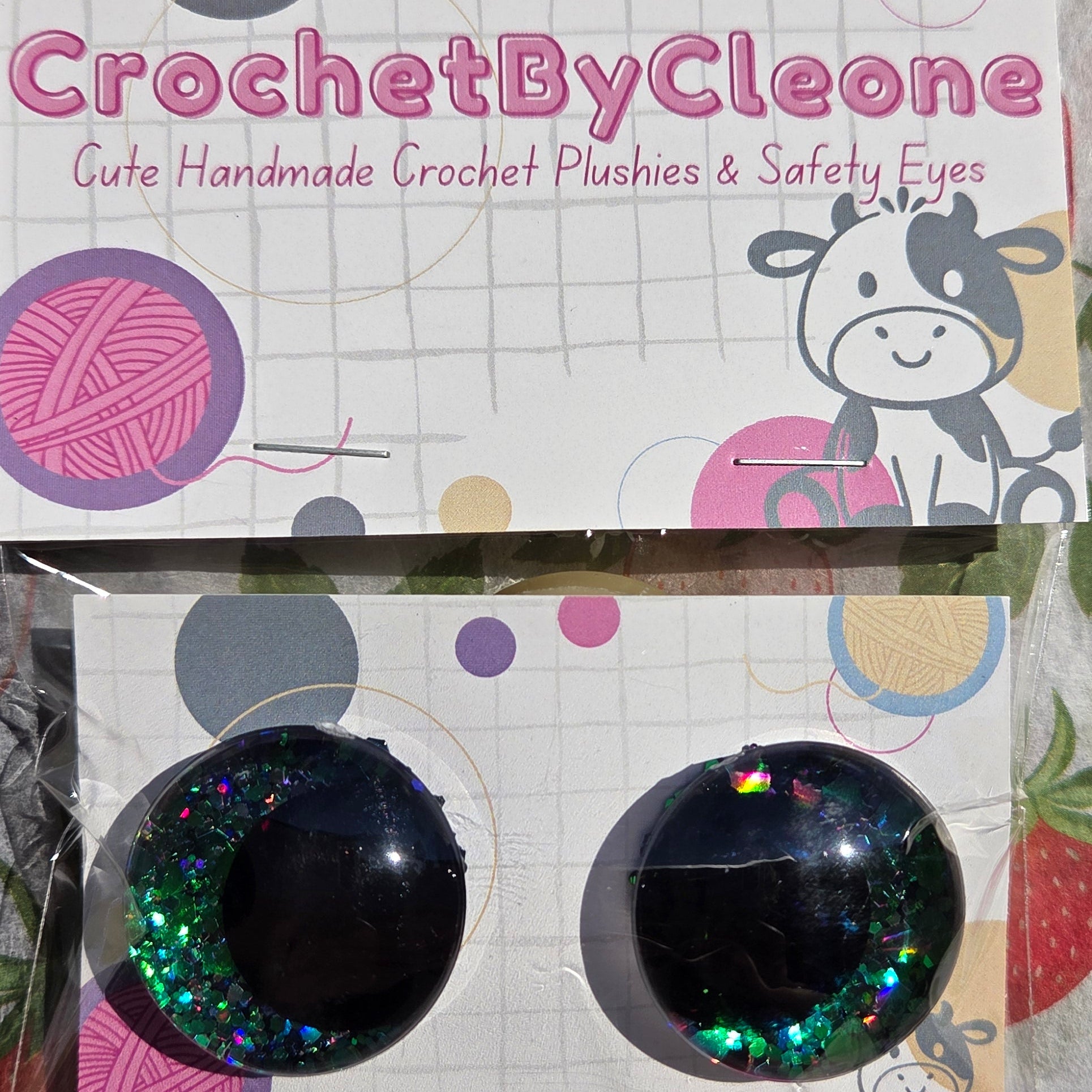 A pair of handmade crochet push-on earrings displayed on branded cards. The earrings are black with one side featuring iridescent green glitter and the other side plain black.