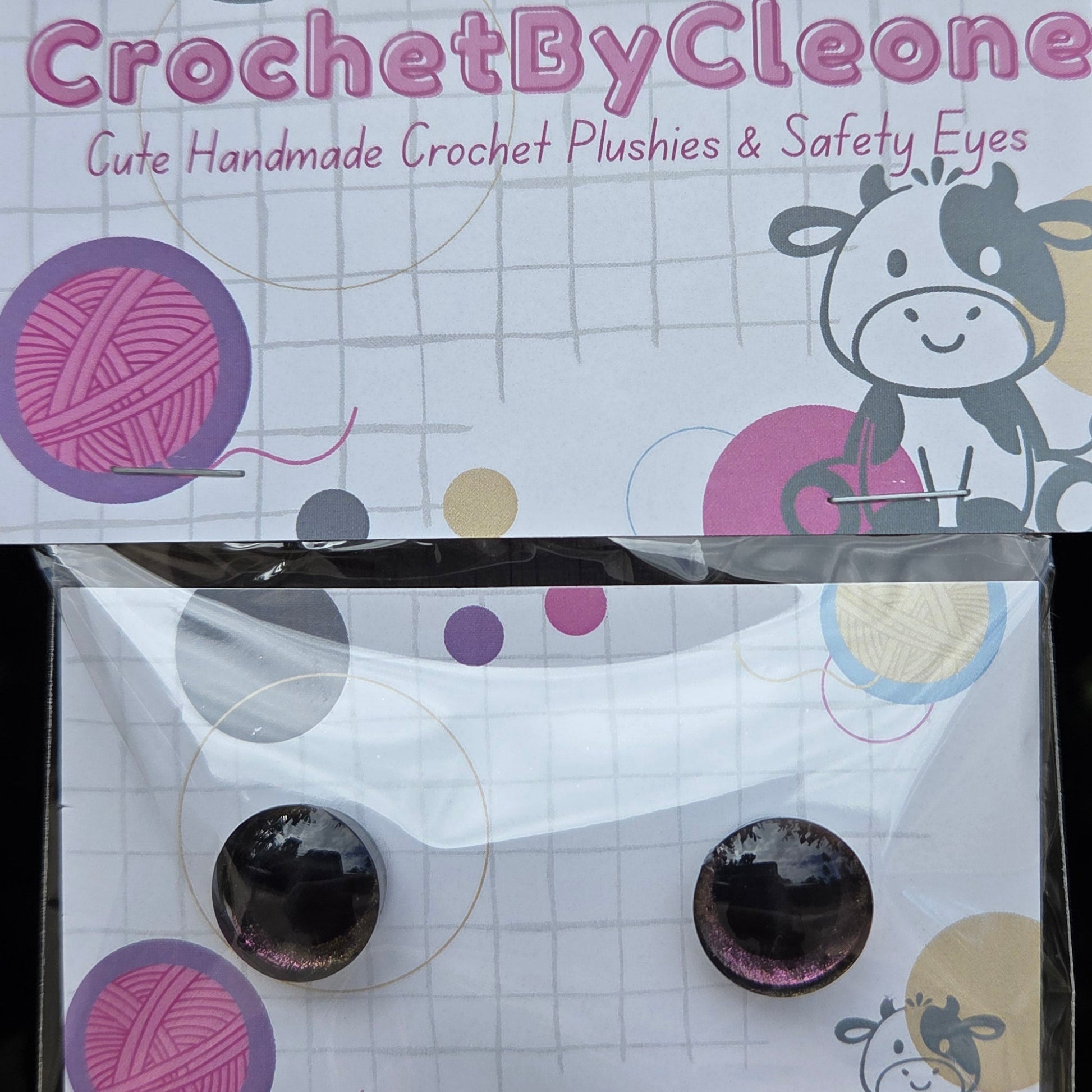 A pair of handmade crochet plushies in a clear plastic bag with a printed backing card. The backing card reads 'CrochetByCleone' and features a cow illustration and yarn ball graphics.