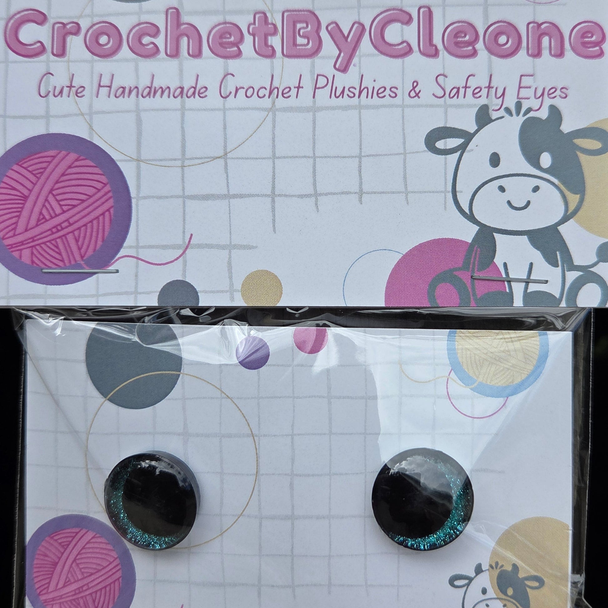 Two packaged crochet crochet eyes on a printed card, photographed on a rustic wooden surface. The left card reads 'CrochetByCleone' and shows decorative yarn-ball graphics; the right package contains two round black-and-silver glittery crochet eyes in clear plastic.