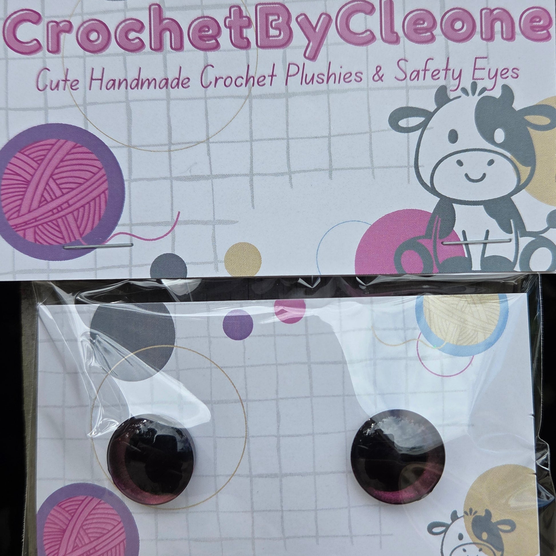 Two packaged crochet plushies displayed on branded backing cards. One plushie is visible on the left card, and the right card shows two round dark plush eyes inside clear plastic packaging.