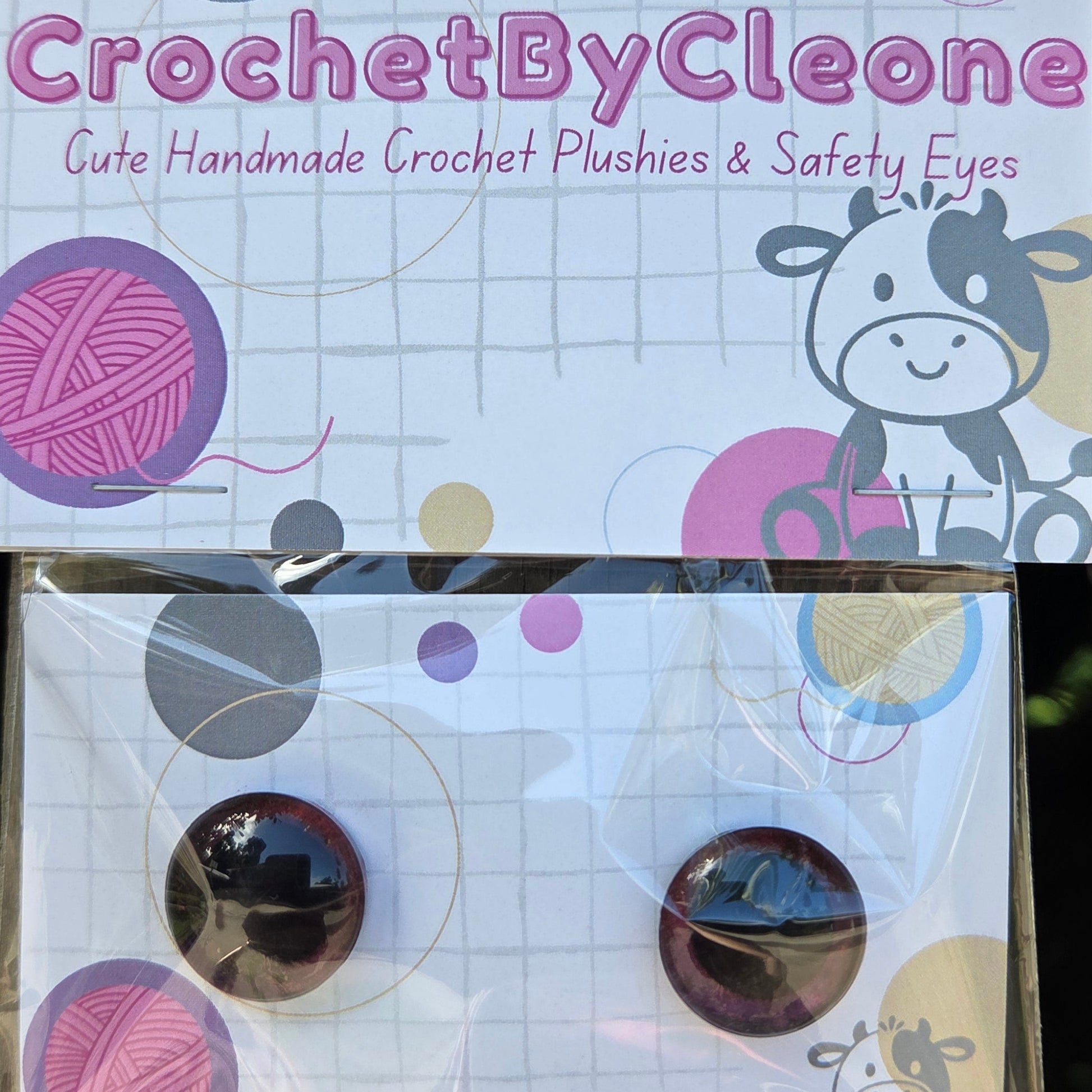 CrochetByCleone handmade crochet plushies and safety eyes displayed on branded packaging cards, resting on a rustic wooden surface.