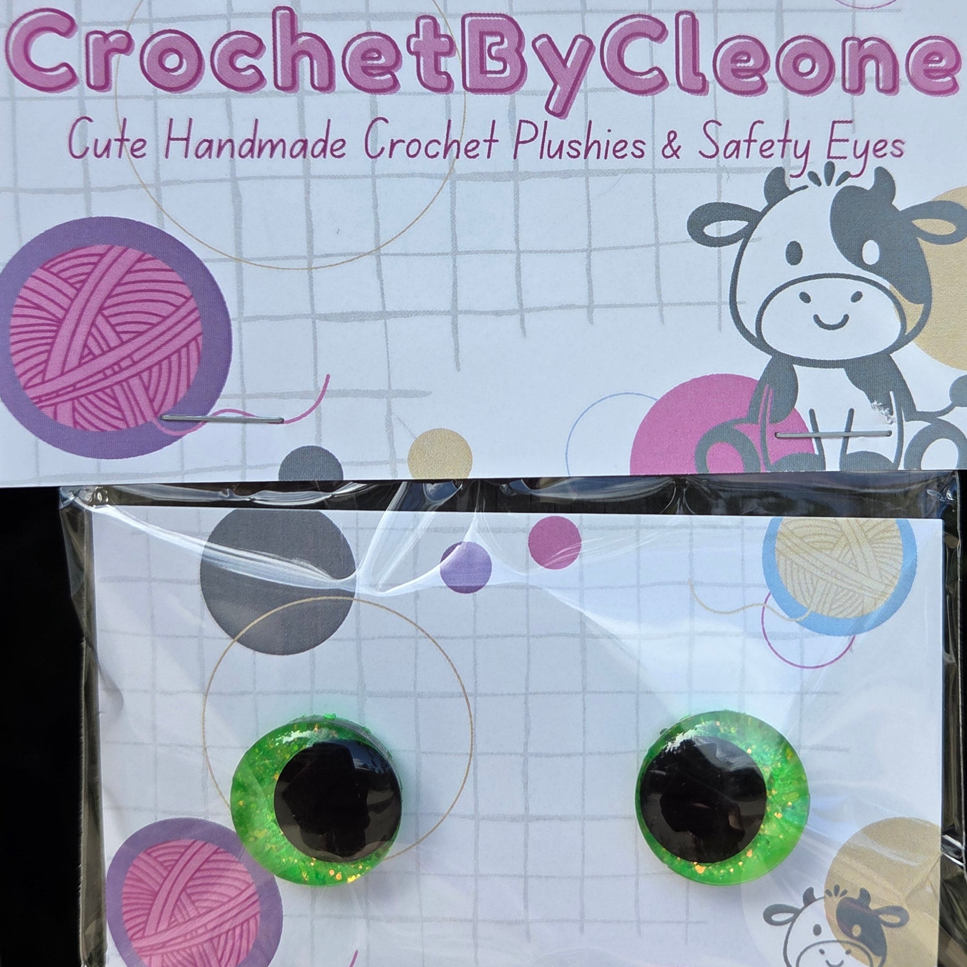 A pair of handmade green glittery safety eyes with black centers, packaged on a branded card that reads 'CrochetByCleone' and says 'Gute Handmade Crochet Plushies & Safety Eyes,' photographed against a rustic wooden background.