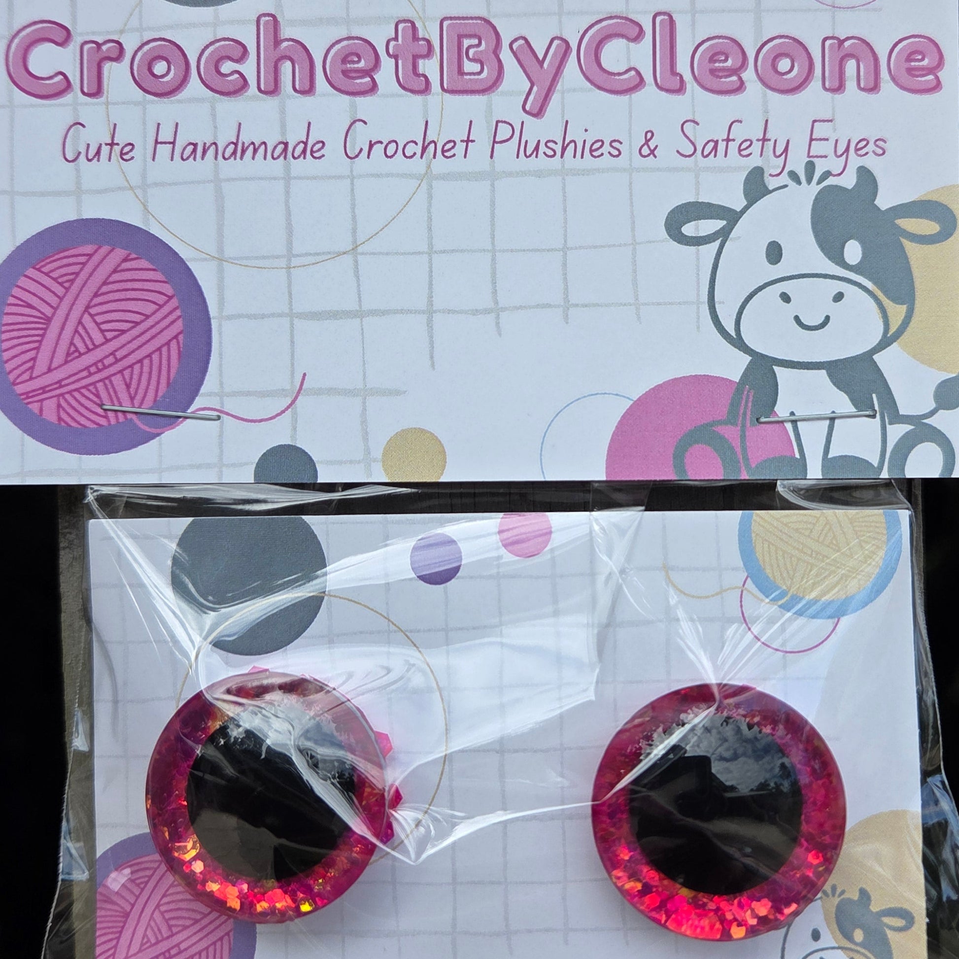 CrochetByCleone handmade crochet plushies and safety eyes displayed on branded backing cards, set against a rustic wooden background.