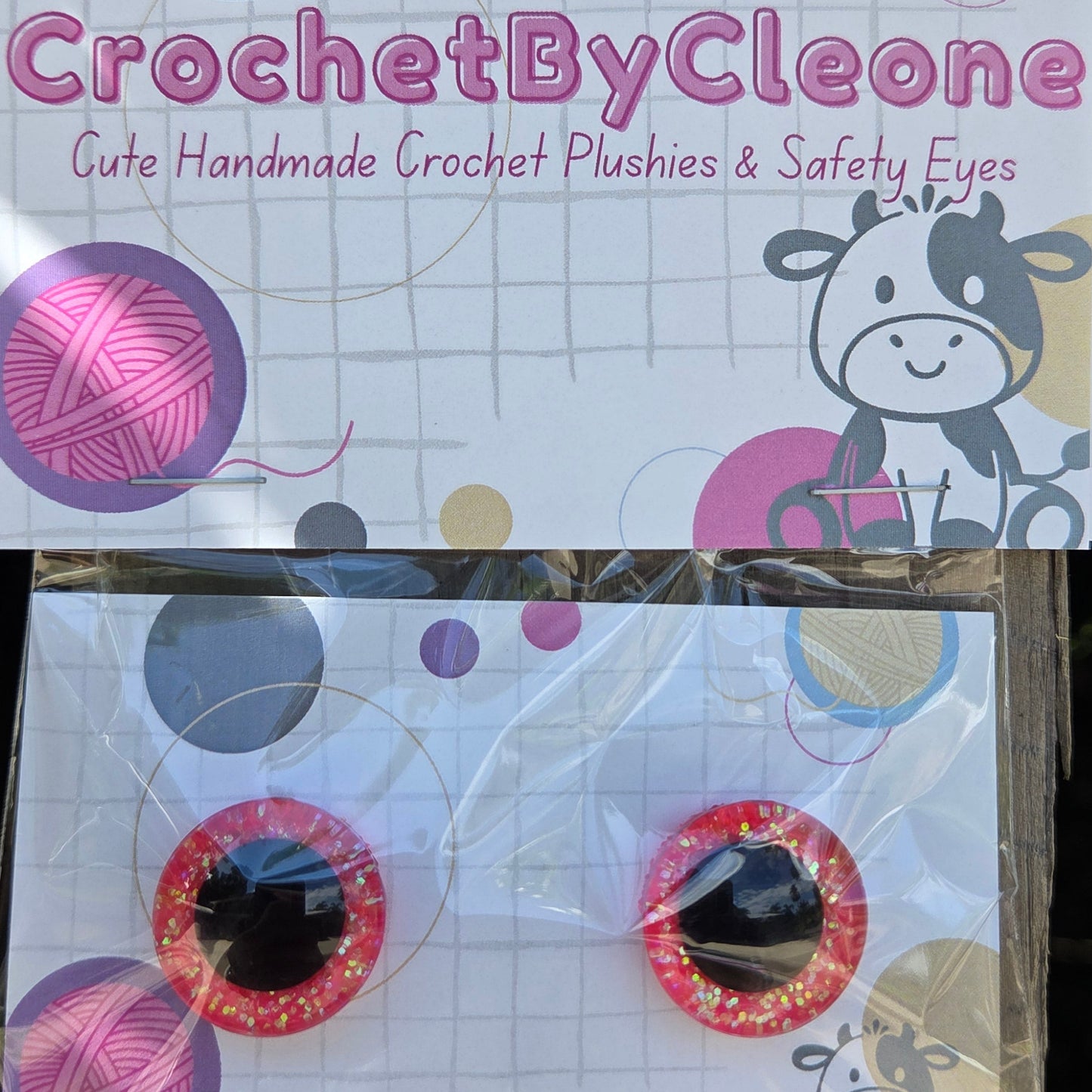 Two novelty crochet crochet plushies and safety eyes packaged on branded cards, displayed on a rustic wooden surface.