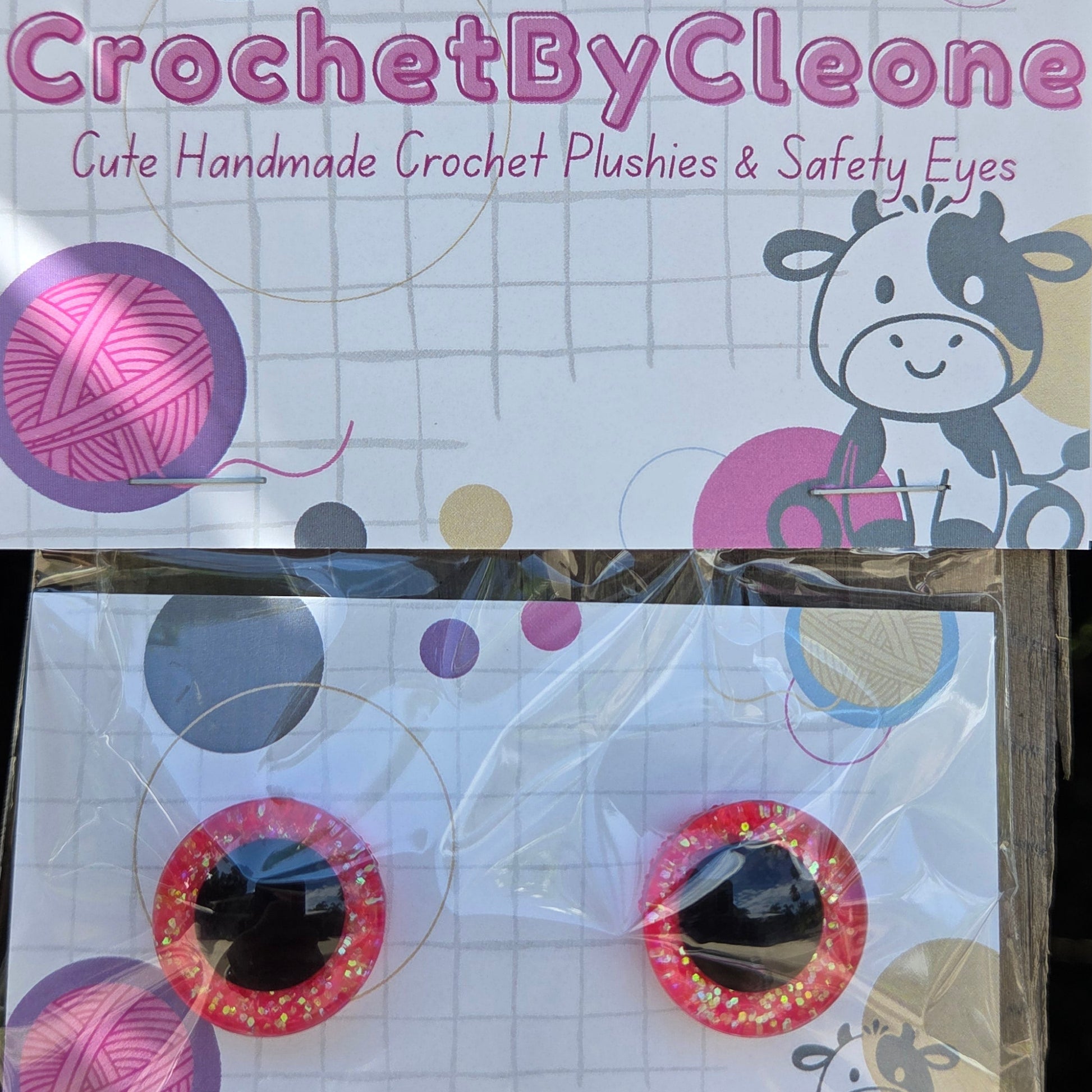 Two novelty crochet crochet plushies and safety eyes packaged on branded cards, displayed on a rustic wooden surface.