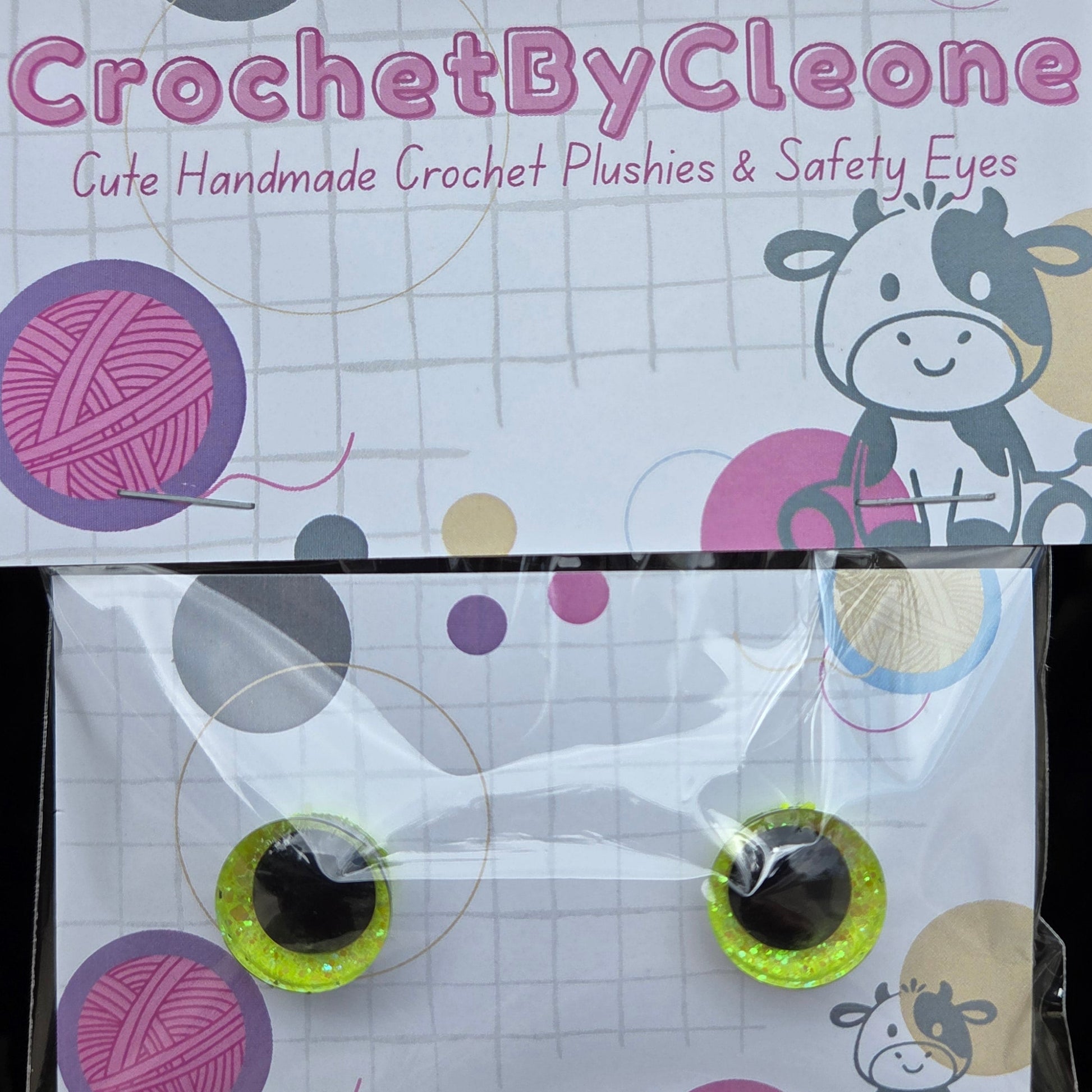 A pair of handmade crochet plushies with safety eyes, packaged in a clear plastic bag with a branded cardboard backing card. The card features the brand name 'CrochetByCleone' and a cartoon cow illustration.