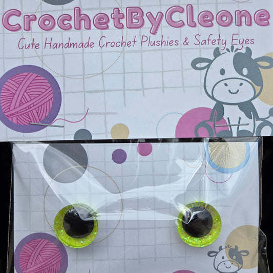 A pair of handmade crochet plushies with safety eyes, packaged in a clear plastic bag with a branded cardboard backing card. The card features the brand name 'CrochetByCleone' and a cartoon cow illustration.